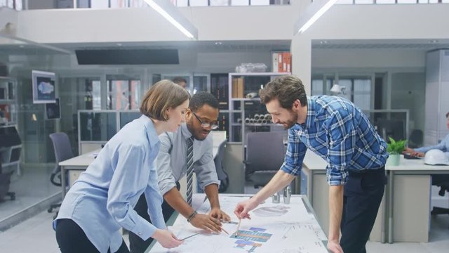 In the Industrial Engineering Facility: Female Designer Works with Industrial Engineer and Master Technician, They have Discussion, Analyse Engine Design Technical Drafts that are Lying on the Table