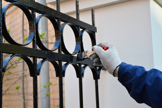 Worker paints a fence in black