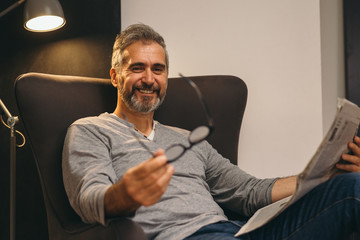 middle aged man reading newspaper relaxed in his sofa at home