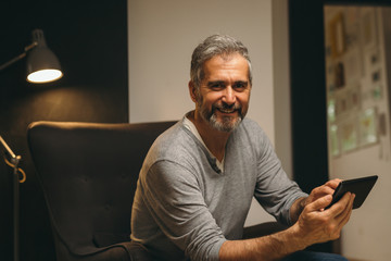 portrait of bearded middle aged man using cellphone relaxed in sofa at his home