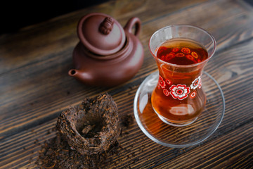 Black tea in traditional turkish tea cup with pattern on wooden table, traditional clay teapot with Puer tea near on wooden table. Black background. Horizontal image.