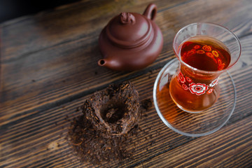 Black tea in traditional turkish tea cup with pattern on wooden table, traditional clay teapot with Puer tea near on wooden table. Black background. Horizontal image.