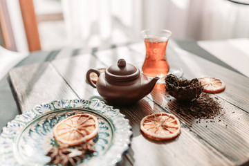 Black tea in traditional turkish tea cup with pattern on wooden table, traditional clay teapot with Puer tea, orange chips near on wooden table. Shallow focus. Horizontal image.