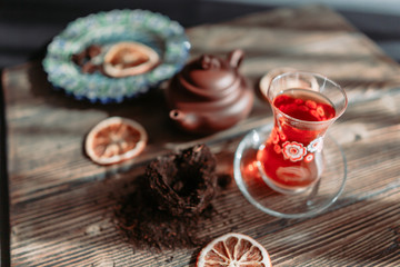 Black tea in traditional turkish tea cup with pattern on wooden table, traditional clay teapot with Puer tea, orange chips near on wooden table. Shallow focus. Horizontal image.