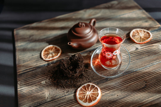 Black tea in traditional turkish tea cup with pattern on wooden table, traditional clay teapot with Puer tea, orange chips near on wooden table. Shallow focus. Horizontal image.