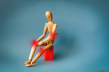 Joint pain concept. The wooden man holds his hands on sore red knee.