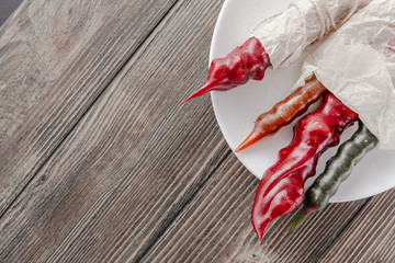 Ancient Georgian national sweet churchkhela, different colours, in white cooking paper on the white plate. Horizontal image. Wooden background.  Top view, flat lay. Copy space.
