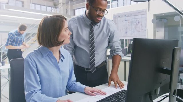 In the Industrial Engineering Facility: Portrait of the Smart and Beautiful Female Engineer Working on Desktop Computer, Her Supervisor Gives Useful Advice about Project Details. 
