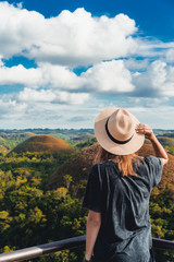 Fototapeta premium Woman in straw hat standing in front of the Chocolate Hills in the Bohol island in the Philippines. Hills covered in brown grass. Famous touristic place