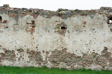 The high resolution texture of the old brick wall with showered plaster and clay putty with green grass. Useful for the texture of the old castle or walls in design, architecture and game development