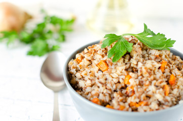 Buckwheat porridge with carrots and parsley in blue plate. On background of Golden onions and green parsley.