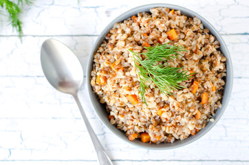 Buckwheat porridge with carrots and dill, top view on a light background.