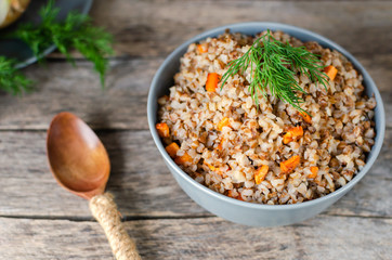 Buckwheat porridge with carrots and dill on an old wooden background.