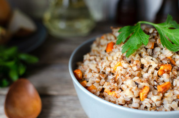 Buckwheat porridge with carrots and parsley in blue plate. On background of Golden onions,green parsley and salt and pepper mills.