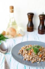 Buckwheat porridge with carrots and parsley in blue plate. On background of Golden onions,green parsley and salt and pepper mills.
