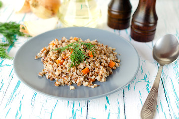 Buckwheat porridge with carrots and parsley in blue plate. On background of Golden onions,green parsley and salt and pepper mills.