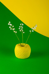 Lily of the valley flowers in a ball of thread on colored background