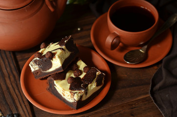 Brownie with cheesecake on a rustic saucer on a wooden background. A cup of coffee on a wooden background