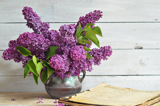 Vase with purple lilac flowers on a light wooden background