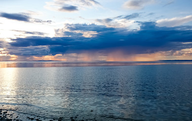 Sunset on Lake Baikal. Evening, rain, clouds, sun. Dramatic sky. Atmospheric landscape. The shore of Lake Baikal. Russia.