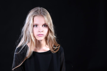 Fototapeta premium Portrait of a blonde girl with long hair on a black background. Emotional portrait.The girl shows different emotions on the face. Plays with long hair.