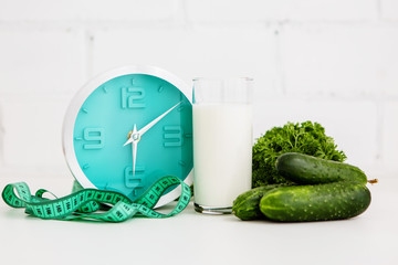 alarm clock with measuring tape glass of kefir and cucumbers on white background, Healthy lifestyle, body slimming and weight loss concept.space for text