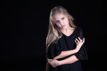 Portrait of a blonde girl with long hair on a black background. Emotional portrait.The girl shows different emotions on the face. Plays with long hair.