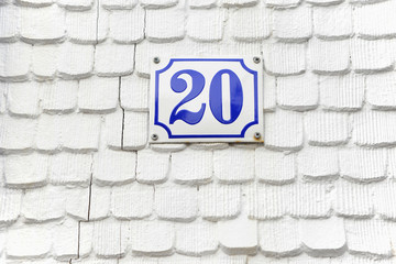 Fototapeta na wymiar Hausnummer 20 aus emailliertem Blech an einer mit weiß gestrichenen alten handgefertigten Holzschindeln verkleideten Hauswand
