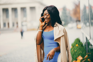 Elegant black woman standing in a autumn city. Businesswoman in a blue dress. Lady use the phone