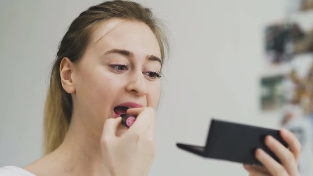 Woman applying lipstick on her lips in front of the mirror