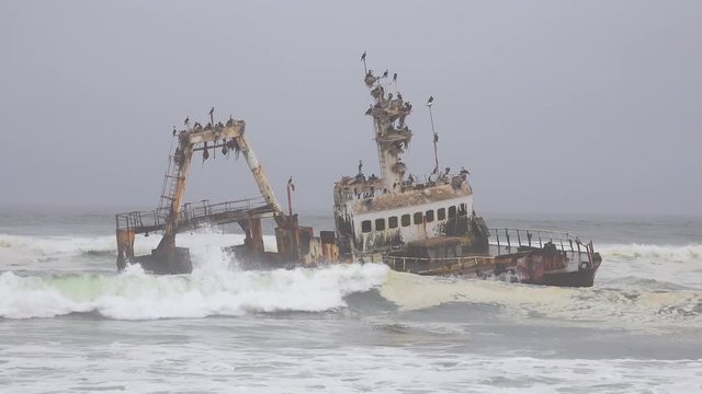 A spooky shipwreck grounded fishing trawler sits in Atlantic waves along the Skeleton Coast of Namibia.