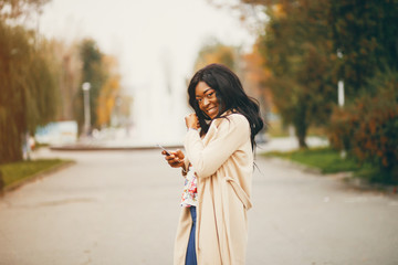 Elegant black woman standing in a autumn city. Businesswoman in a long coat. Lady use the phone