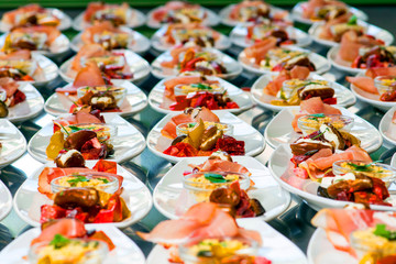 Fototapeta na wymiar Caterer puts the starter on many plates with vegetables and antipasti
