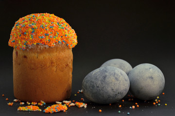 Easter cake with eggs colored by hibiskus tea on black background in beam of light, among sugar crumbs, with copyspace © Mykola