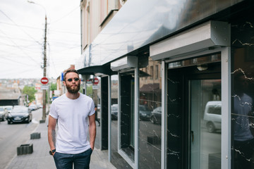 Fototapeta na wymiar Handsome hipster man in sunglasses walking along the street. White t-shirt.