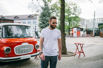Handsome hipster man in sunglasses walking along the street. White t-shirt.