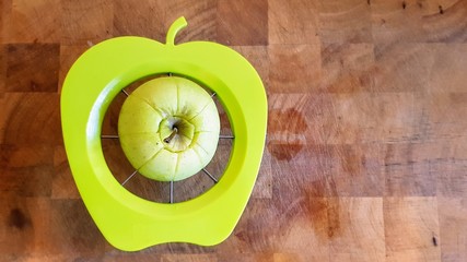 A green apple being separated into chunks by a green apple shaped slicer, divider and corer on a wooden butchers block.