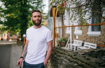 Handsome hipster man in sunglasses walking along the street. White t-shirt.