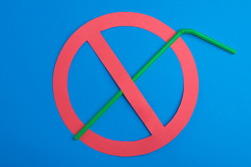Green plastic straw set up in a red prohibition circle over a blue background, telling a campaign...