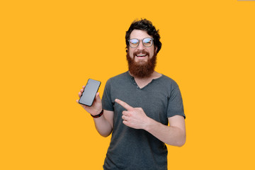Photo of handsome bearded guy  pointing at his mobile while looking at camera