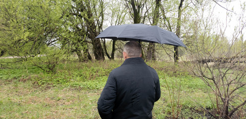Elderly man with a black umbrella in nature.