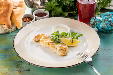 White fish fillet baked with lemon slice and white sauce on blue wooden table