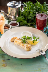 White fish fillet baked with lemon slice and white sauce on blue wooden table