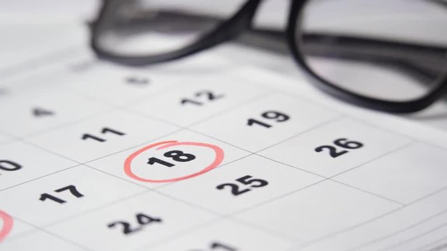 Signing a day on a calendar with red pen or marker. Putting date in circle.