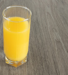 A glass of orange juice on a wood-textured surface.