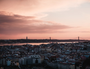 view of the Alfama downtown and the 25 de Abril Bridge at a dramatic sunset in Lisbon, Portugal