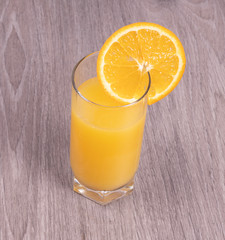 A glass of orange juice with a slice of orange on a wooden textured background
