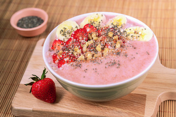 Breakfast smoothie bowl with banana, strawberries, chia seeds and cinnamon on a wooden cutting board