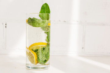 summer cooling drink. a glass of lemonade on a light background. glass of water with lemon and mint