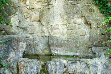 water for drinking flows from old stones with green leaves close up